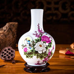 Vase en porcelaine blanche décoré de motifs floraux colorés et d'un oiseau, posé sur un socle en bois sombre.