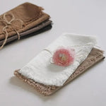 Un étui en tissu délicat et une fleur rose sur un fond clair.