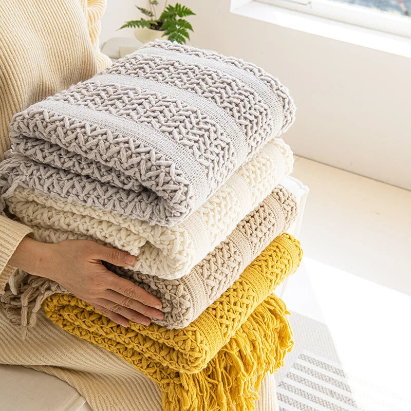 Une pile de plaids moelleux et colorés, dans des tons naturels et neutres, créant une atmosphère chaleureuse et accueillante.