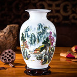Un vase de porcelaine blanche décoré d'un paysage montagneux aux couleurs vives, avec une petite cabane en bois au premier plan, entouré d'éléments naturels tels que des arbres et des rochers.