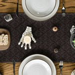 Une table de salle à manger avec des assiettes, des couverts et des éléments de décoration, sur un fond de motif sombre, créant une ambiance chaleureuse et conviviale.