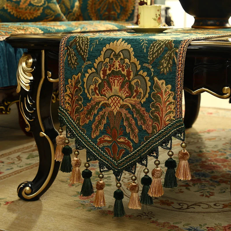 Magnifique chemin de table décoratif aux motifs floraux ethniques dorés et verts sur un fond bleu marine, orné de franges élégantes.