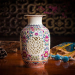 Vase en porcelaine décoré de motifs floraux, avec une ouverture ajourée et un design élégant posé sur une table en bois.