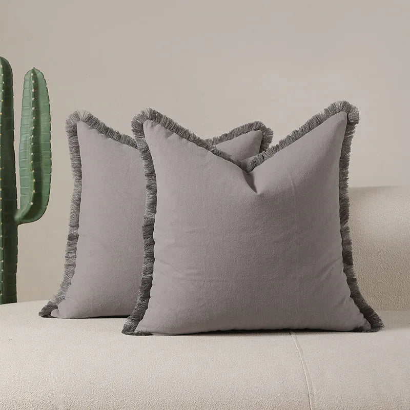 Deux oreillers gris décoratifs avec des franges sur fond de cactus verts.