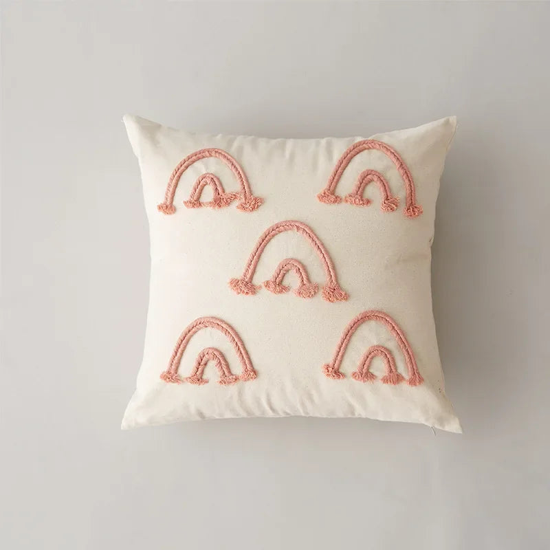 Coussin décoratif blanc avec des arcs-en-ciel roses brodés sur toute la surface.