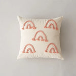 Coussin décoratif blanc avec des arcs-en-ciel roses brodés sur toute la surface.