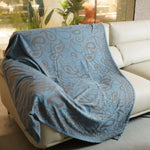 Couverture décorative pliée avec un motif abstrait bleu sur fond blanc, créant une atmosphère apaisante dans une pièce ensoleillée.