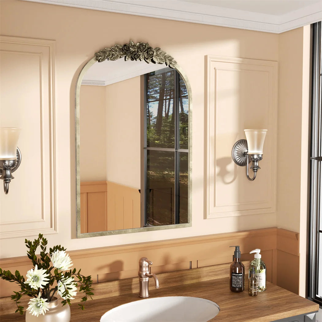 Un miroir décoratif avec une bordure florale se trouve dans une salle de bain lumineuseaccompagné de décors floraux et d'accessoires de toilette.