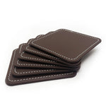 Un ensemble de sous-verres en cuir marron avec coutures apparentes, disposés en pile sur fond blanc.