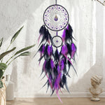 Un attrape-rêves violet et noir suspendu au mur, orné de perles et de plumes, évoquant la spiritualité et la méditation.