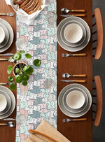 Une table joliment dressée avec des assiettes blanches, des couverts en bois et une nappe aux motifs colorés, mettant en valeur un arrangement végétal frais et harmonieux.
