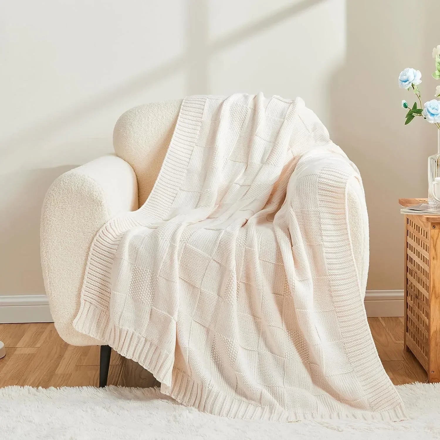 Cette image montre une couverture en tricot douillette et confortable posée sur un fauteuil moelleux, dans un intérieur chaleureux et lumineux.