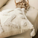 Coussin décoratif en tissu beige doux avec de petits pompons blancs, déposé sur un canapé moelleux.