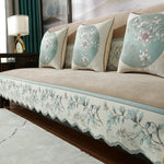 Un canapé moelleux et confortable, avec des coussins ornés de motifs floraux et paysagers dans des tons bleus et beiges, créant une atmosphère relaxante et élégante.
