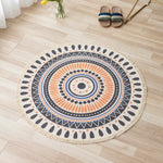 Un tapis rond, motifs ethniques et géométriques, aux tons chauds et contrastés, posé sur un sol en bois clair, complété par des sandales en mailles.