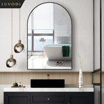 Cette image montre une élégante salle de bain au design moderne, avec un miroir arrondi encadré de noir, des luminaires dorés, une baignoire blanche et un meuble de rangement noir avec un plateau en marbre blanc.