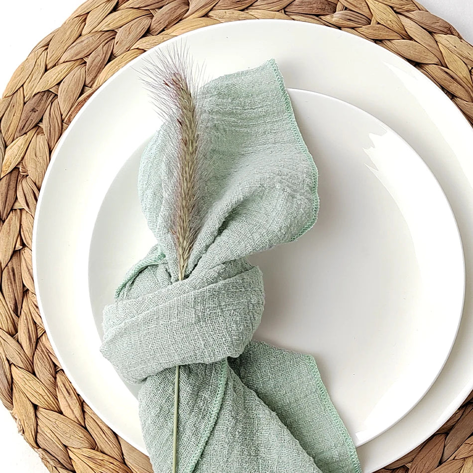 Une serviette de table textile de couleur verte avec un motif texturé, posée sur une assiette blanche sur un napperon tressé.