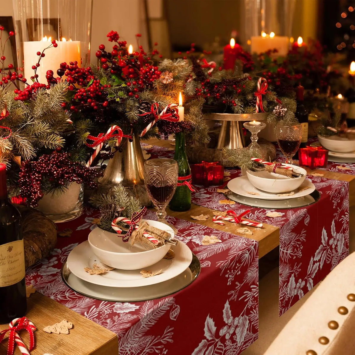 Cette image montre une table joliment décorée pour les fêtes de Noël, avec des ornements rouges, des bougies et un beau centre de table composé de branches de sapin, de baies rouges et d'autres éléments décoratifs.