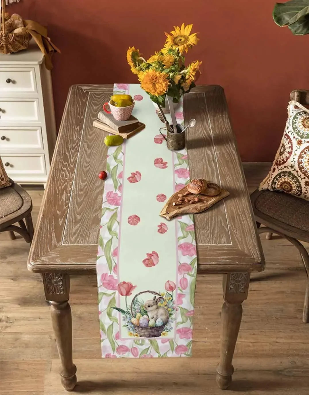 Cette image montre une table en bois décorée avec des fleurs jaunes, des livres, des fruits et un chemin de table fleuri, créant une atmosphère chaleureuse et vintage.