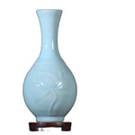 Cette image montre un vase décoratif de couleur bleu clair avec une forme élégante et épurée, posé sur un socle en bois sombre.