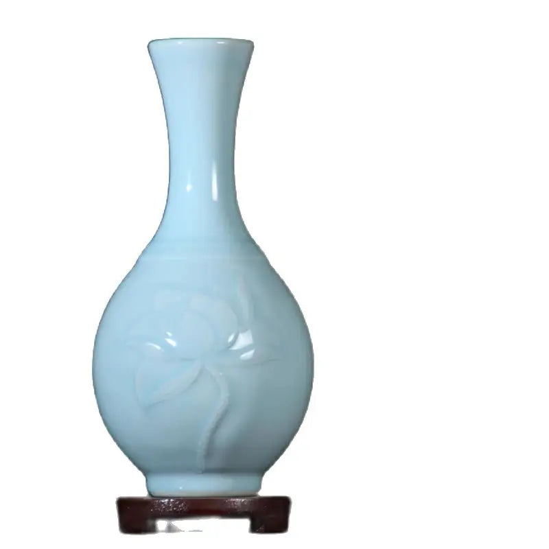 Cette image montre un vase décoratif de couleur bleu clair avec une forme élégante et épurée, posé sur un socle en bois sombre.
