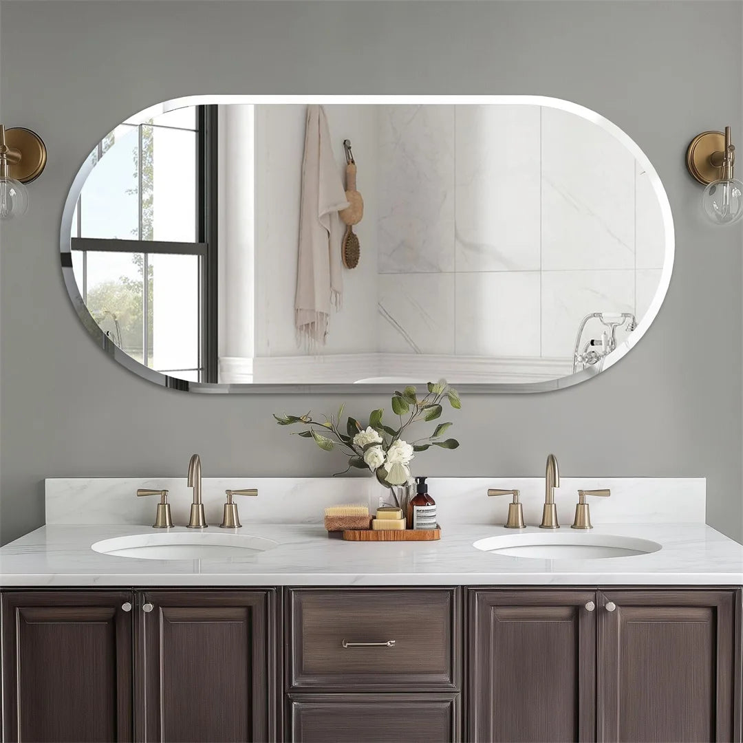 Un grand miroir ovale au-dessus d'un meuble de salle de bain en bois foncé avec deux vasques blanches et des robinets en laiton brossé. Une décoration florale et des accessoires de salle de bain complètent la composition élégante et épurée de cette pièce.