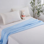 Une chambre douillette avec des draps et des oreillers blancs, une couverture bleue et un adorable lapin en peluche, créant une atmosphère sereine et accueillante.