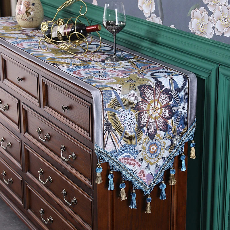 Ce mobilier vintage élégant présente un plateau orné de motifs floraux colorés dans des tons bleu, jaune et beige, rehaussé d'un élégant support en métal doré pour une bouteille de vin et deux verres, offrant une ambiance chaleureuse et raffinée.