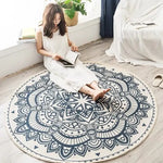 Une femme assise sur un tapis rond orné de motifs décoratifs noirs et blancs, lisant attentivement un livre.