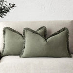 Oreiller décoratif gris avec bord frangé sur un canapé blanc.