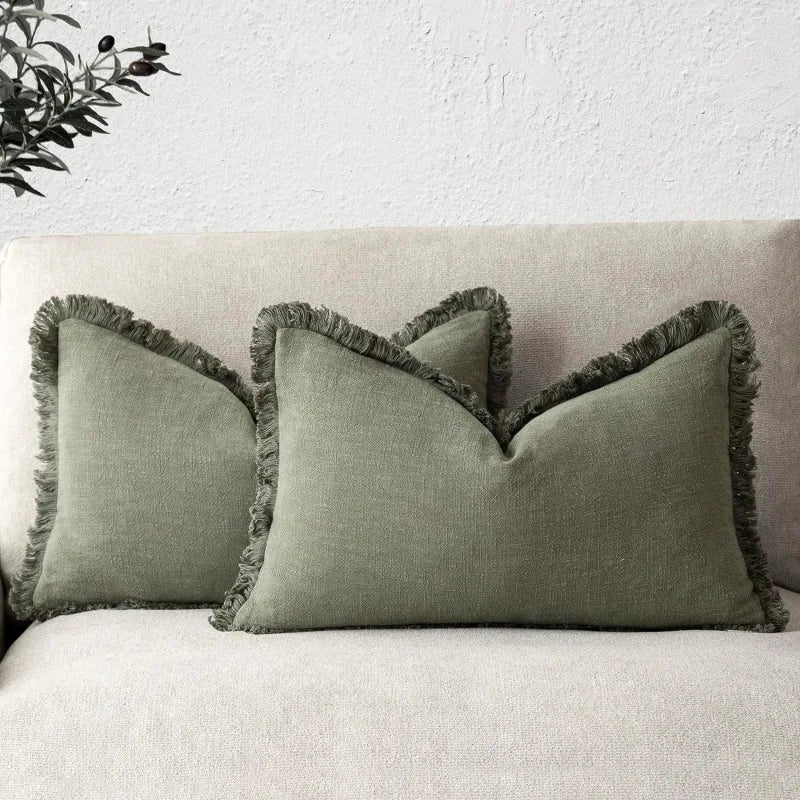Oreiller décoratif gris avec bord frangé sur un canapé blanc.