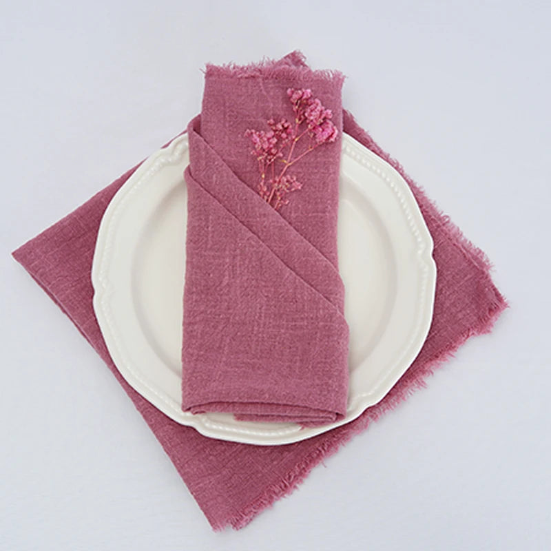 Serviette en lin rose pastel ornée d'une délicate fleur séchée, posée sur une assiette blanche.
