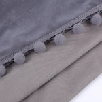 Gros plan sur les finitions pompons gris cousus sur un tissu en velours gris clair, mettant en valeur la texture du rideau.