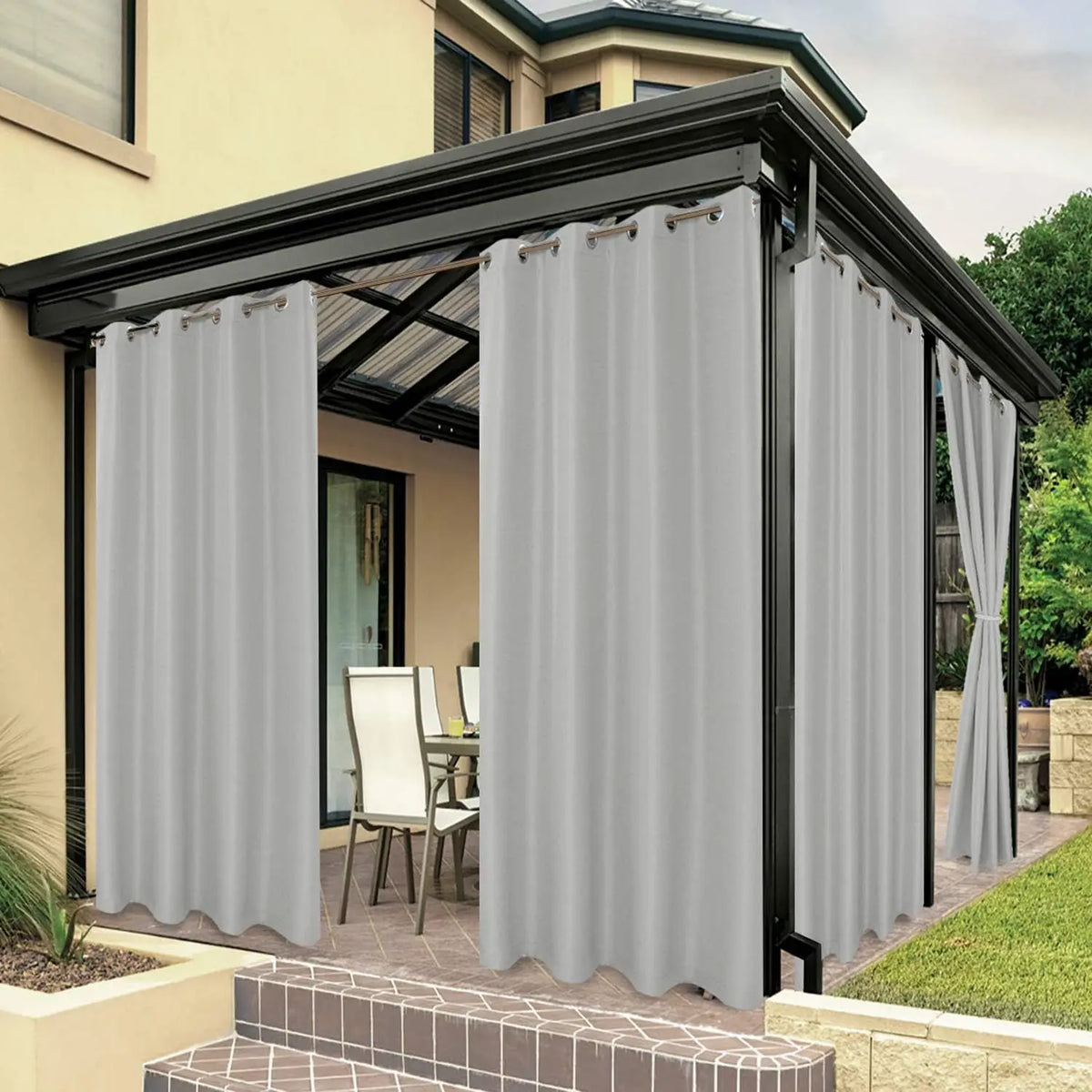 Rideaux d'extérieur gris clair suspendus autour d'une pergola moderne noire, créant un espace repas élégant et protégé sur une terrasse.