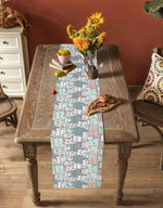 La table en bois vintage est décorée d'un chemin de table motif abstrait aux couleurs douces, avec un bouquet de fleurs jaunes et un encas posé sur le côté.
