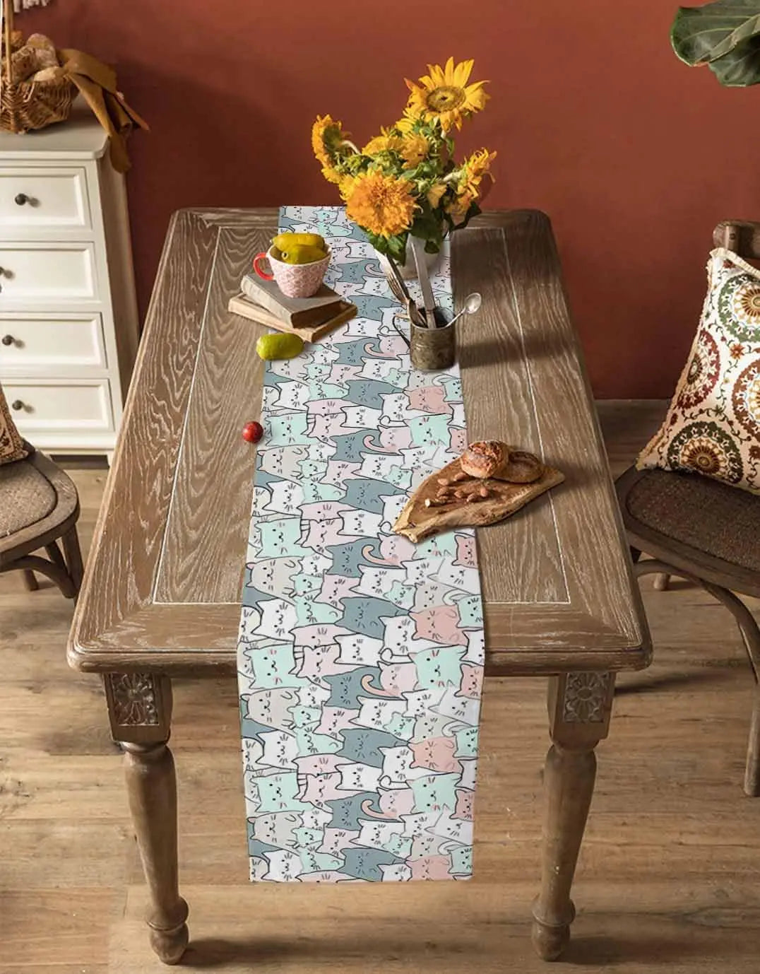 La table en bois vintage est décorée d'un chemin de table motif abstrait aux couleurs douces, avec un bouquet de fleurs jaunes et un encas posé sur le côté.