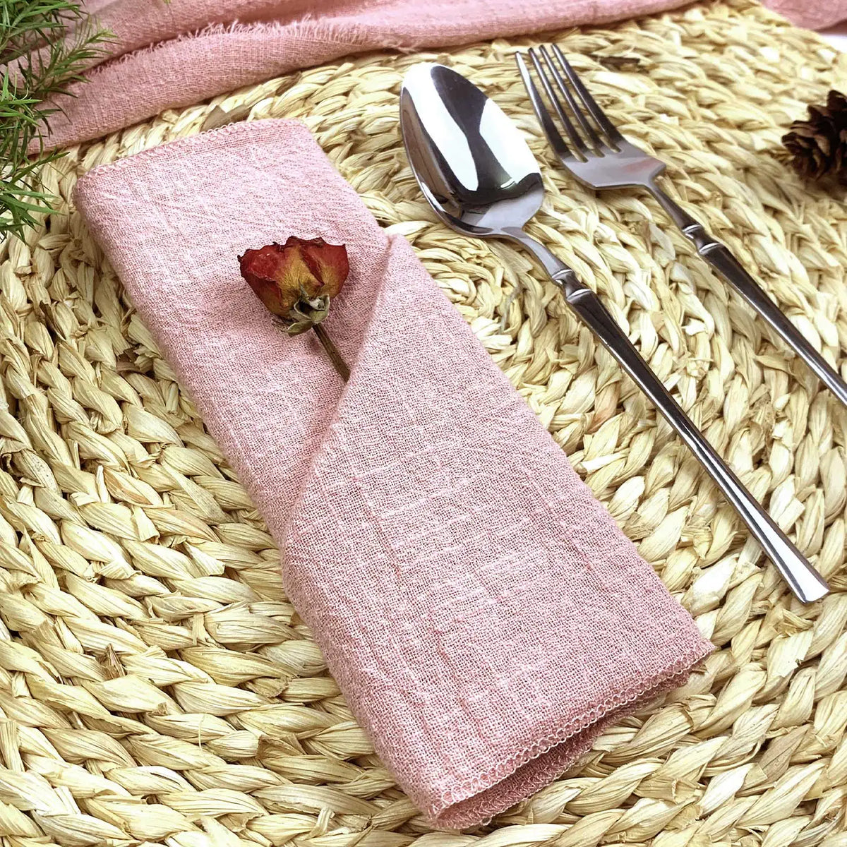 Élégante table de cuisine : une serviette rose pastel avec une rose décorative sur un tapis de jonc tressé avec des couverts argentés.