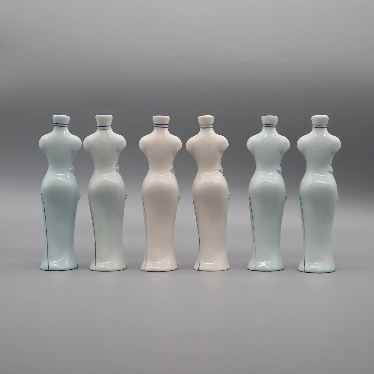 Six bouteilles en céramique blanche et bleu-gris alignées sur fond gris.