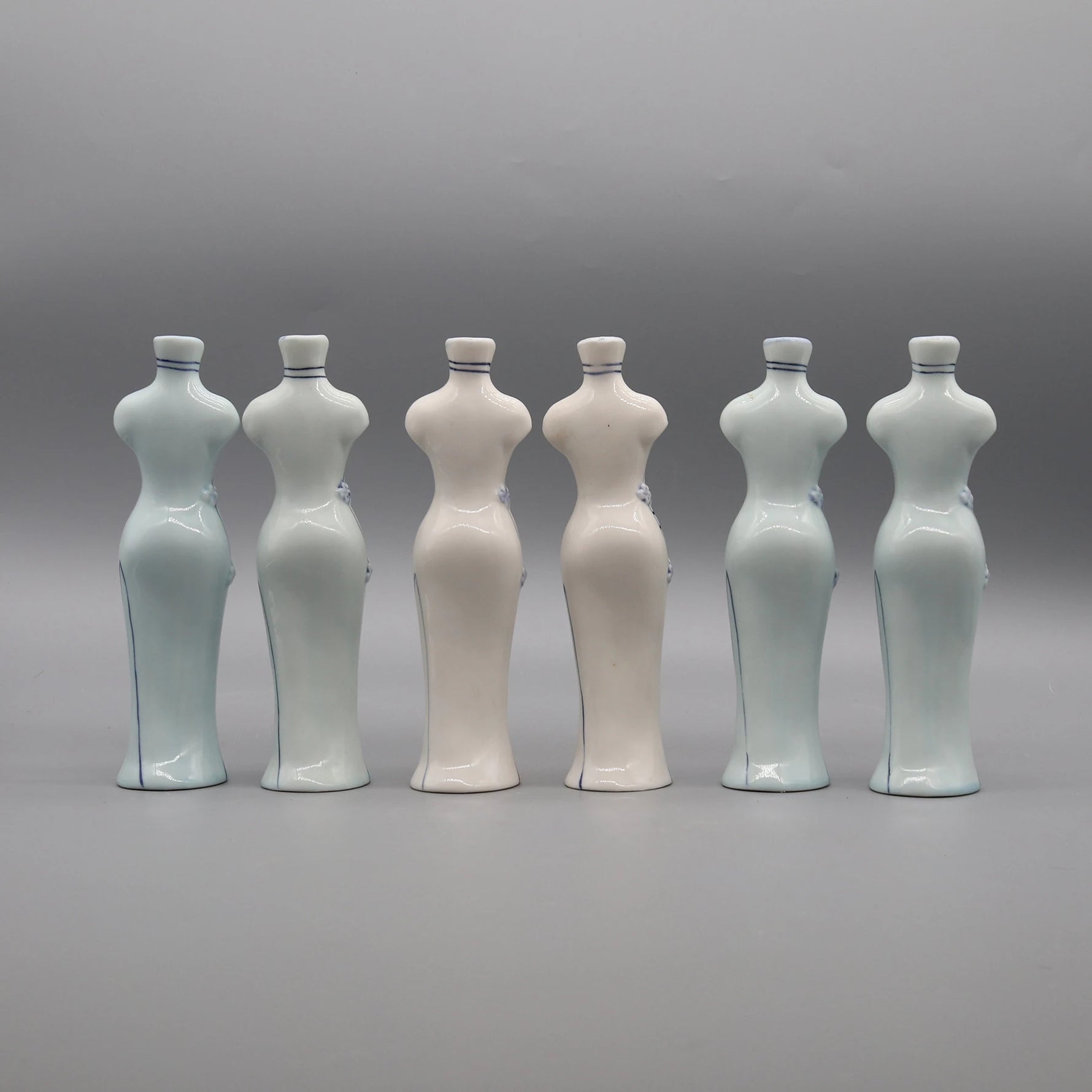 Six bouteilles en céramique blanche et bleu-gris alignées sur fond gris.