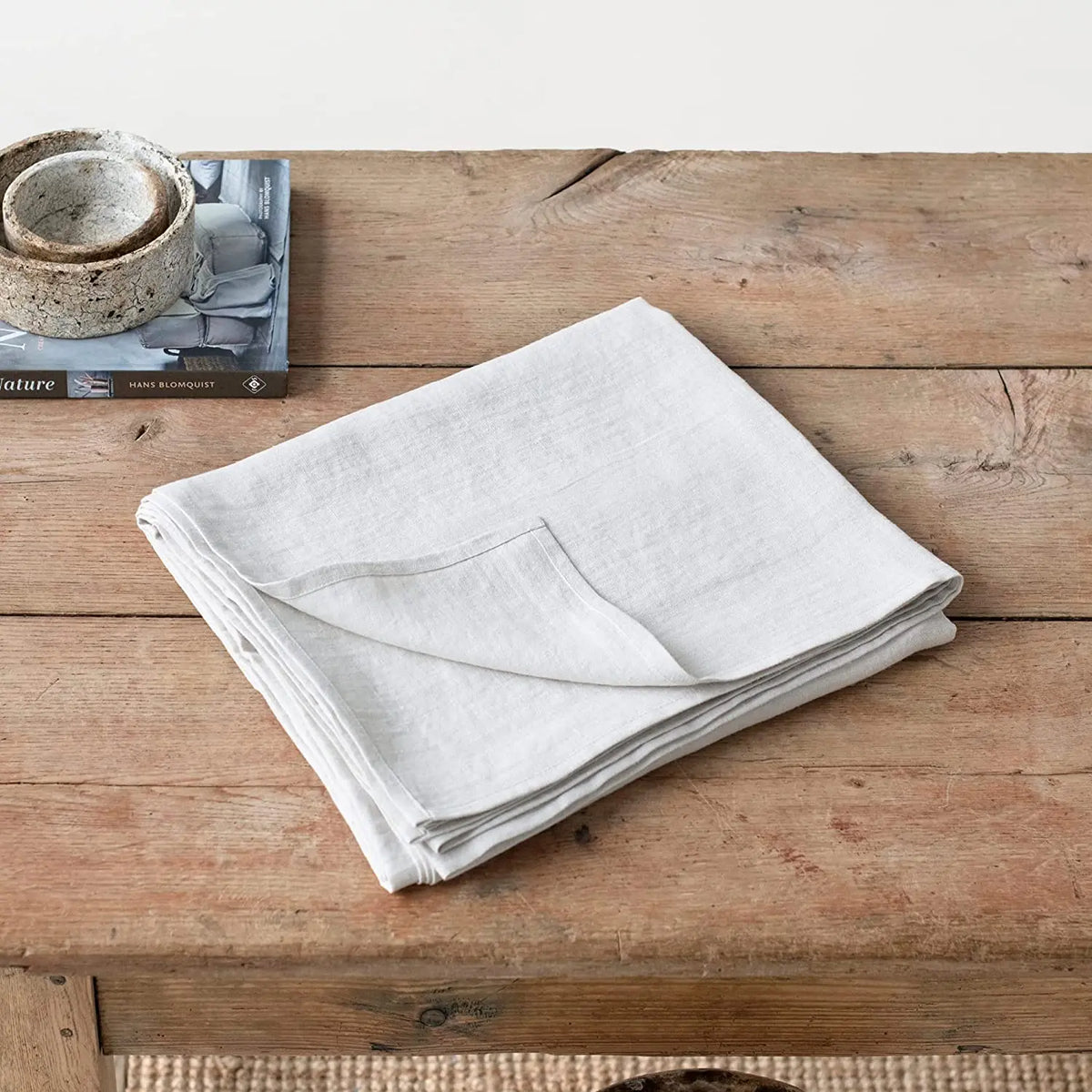 Serviettes blanches en lin épais posées sur une table en bois brut avec des livres et un objet en céramique.