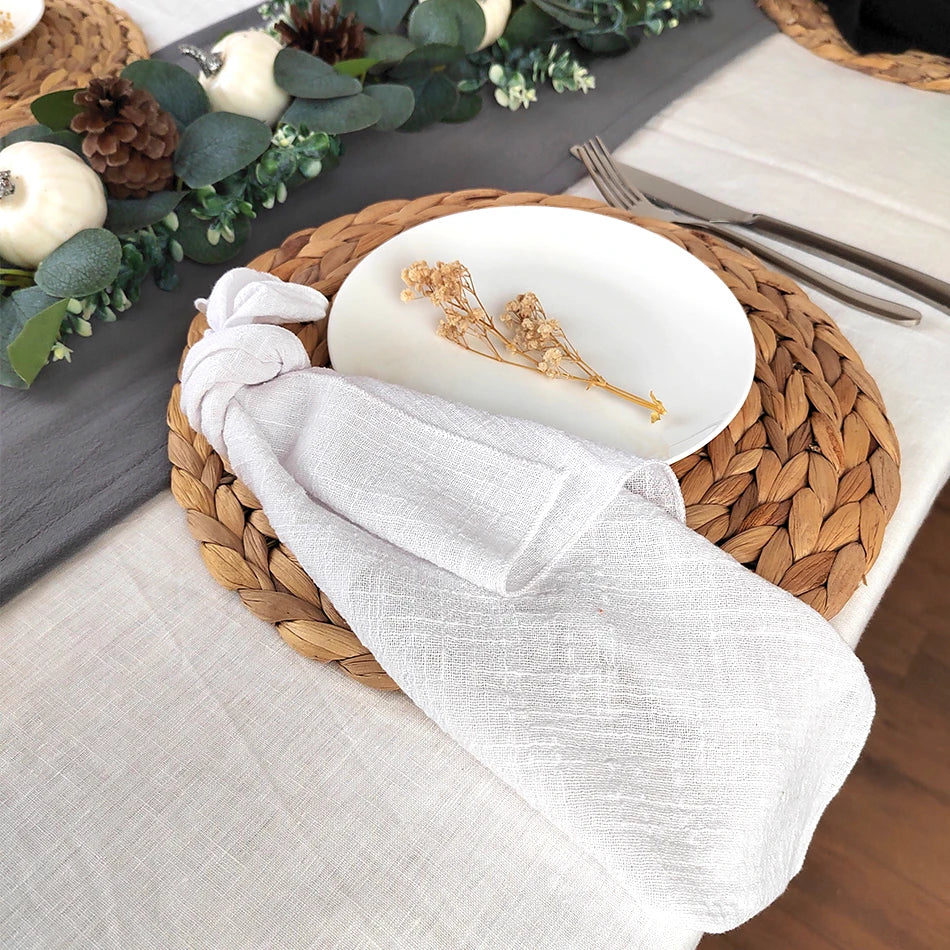 Élégante table de fête avec une assiette blanche, une serviette de lin grise, une couronne de branchages et de pommes de pin, créant une atmosphère chaleureuse et automnale.