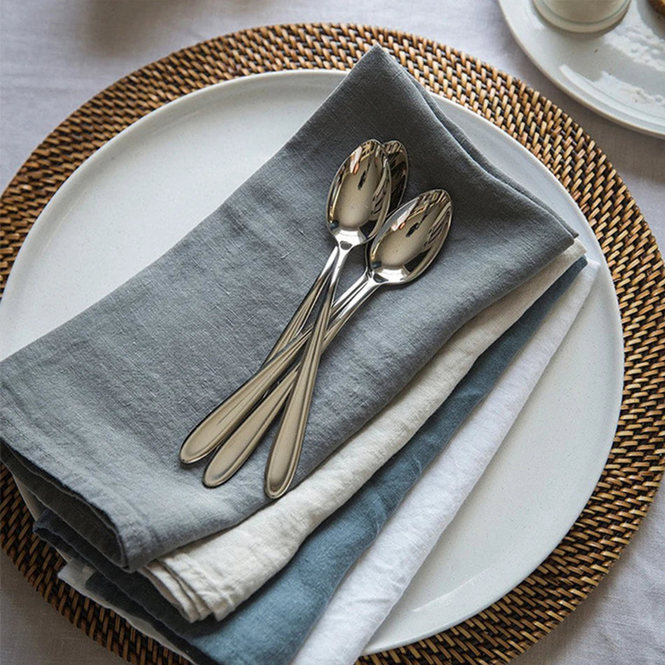 Deux couverts à dessert en métal argenté posés sur un set de table décoré de gris et de blanc.