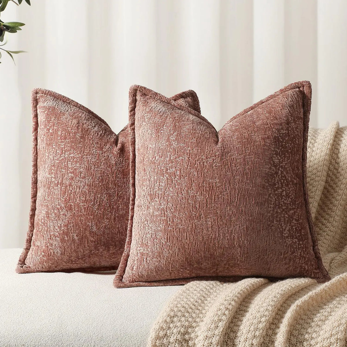 Des coussins en velours brun, texturés et confortables, posés sur un canapé, créant une ambiance chaleureuse et apaisante dans un décor neutre.