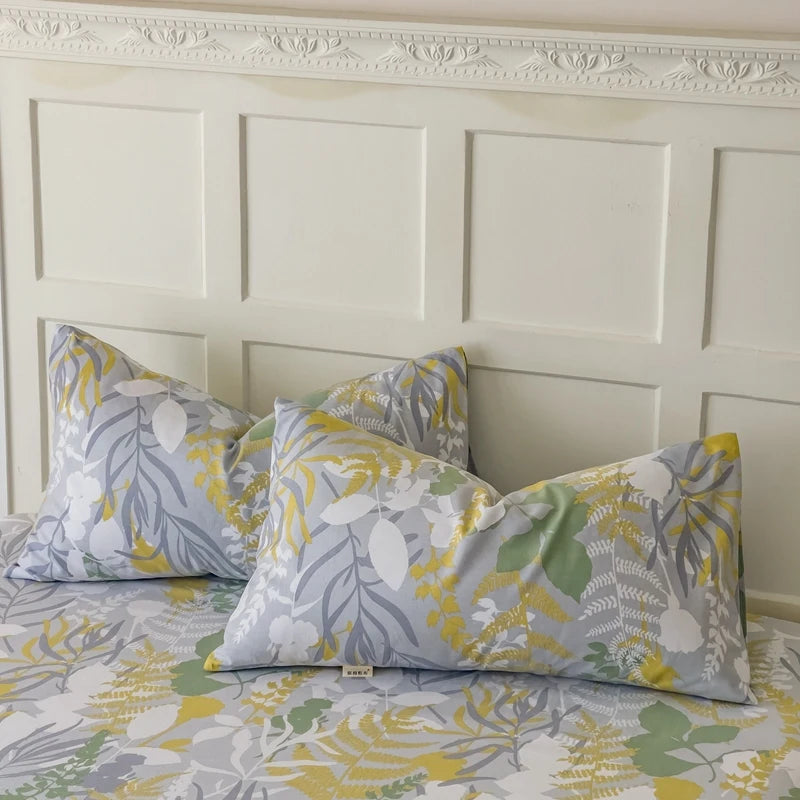 Ensemble de draps et d'oreillers de lit avec un motif floral jaune, gris et vert sur un fond blanc, placé devant un mur avec des panneaux blancs et une moulure décorative.