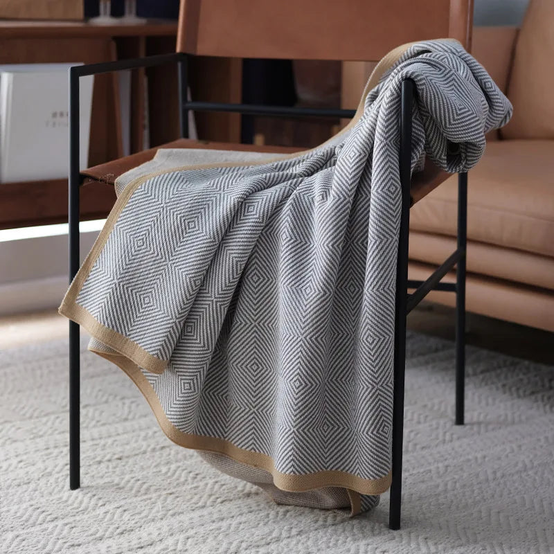 Une couverture grise à motifs de losanges est posée sur une chaise de salon, créant une ambiance chaleureuse et confortable dans la pièce.