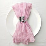Nappe en tulle rose élégante, décorée d'un nœud raffiné avec des plumes noires et blanches, posée sur une assiette blanche.