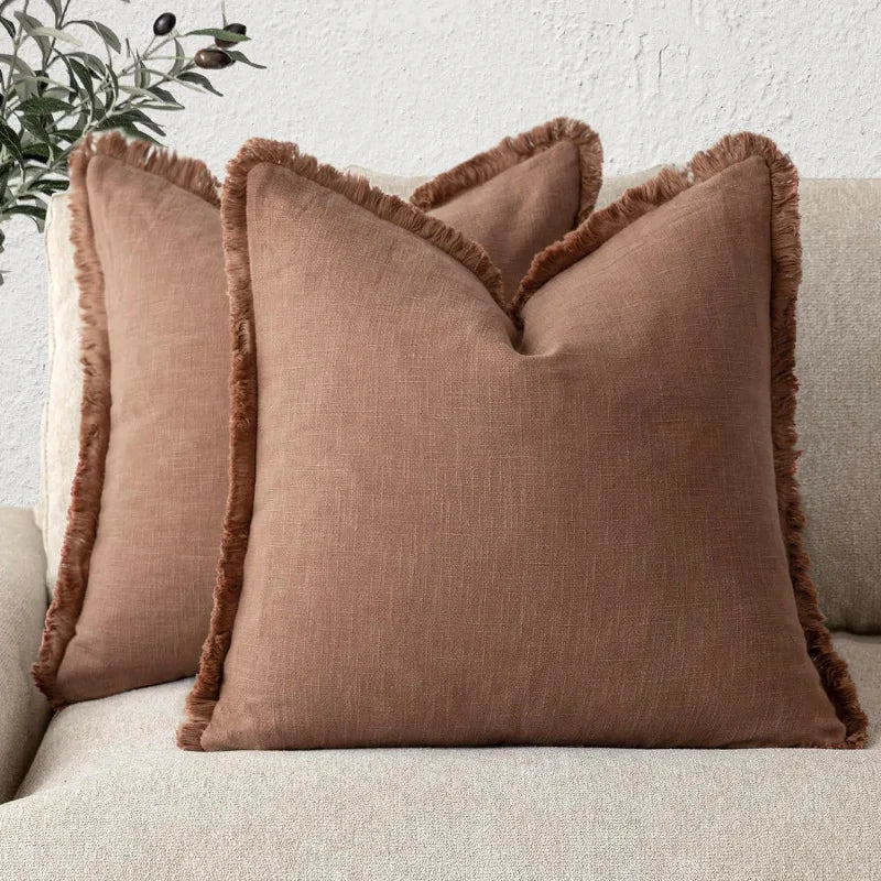 Deux oreillers décoratifs en lin beige frangés posés sur un canapé blanc, créant une ambiance cocooning et chaleureuse.