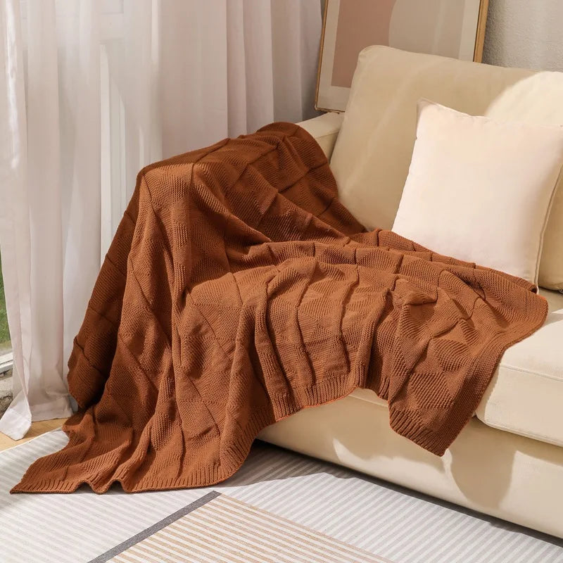 Une couverture de luxe en tricot brun clair, douillette et confortable, reposant sur un canapé aux tons clairs, créant une atmosphère chaleureuse et accueillante dans cet intérieur.