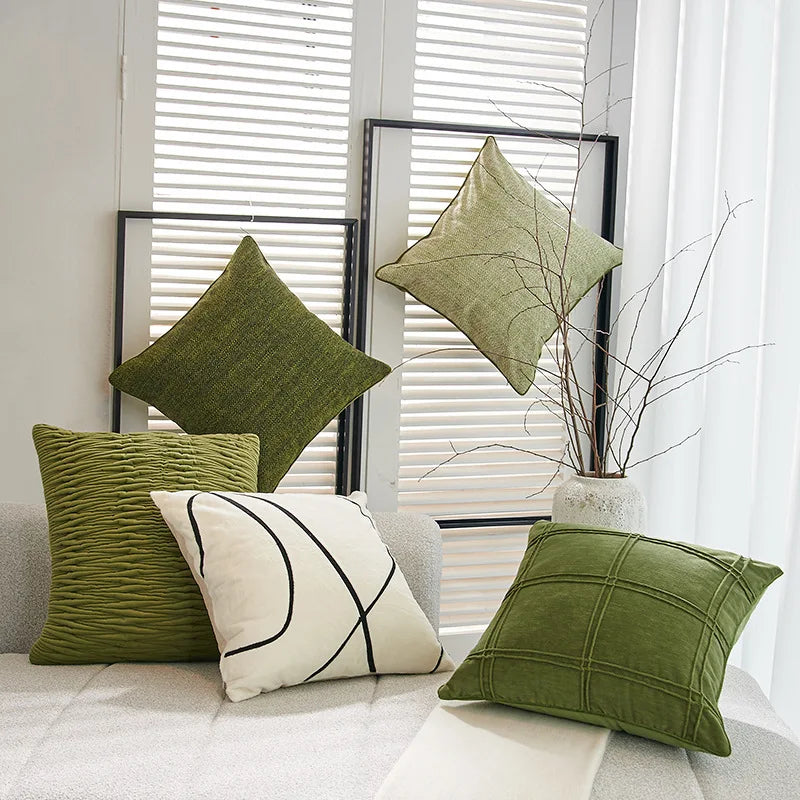 Une variété de coussins décoratifs verts et blancs dans un intérieur moderne avec des stores blancs en arrière-plan.