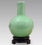 Un vase décoratif de forme sphérique en verre teinté de couleur vert pastel, reposant sur un support en bois sombre.